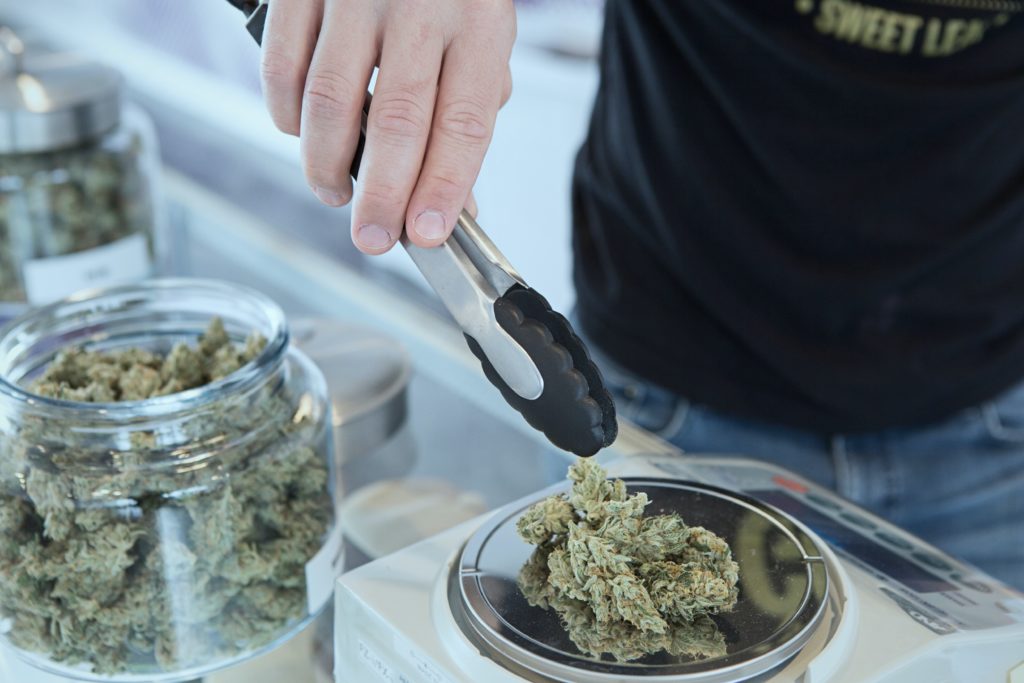 Hand using tongs with big jar of cannabis